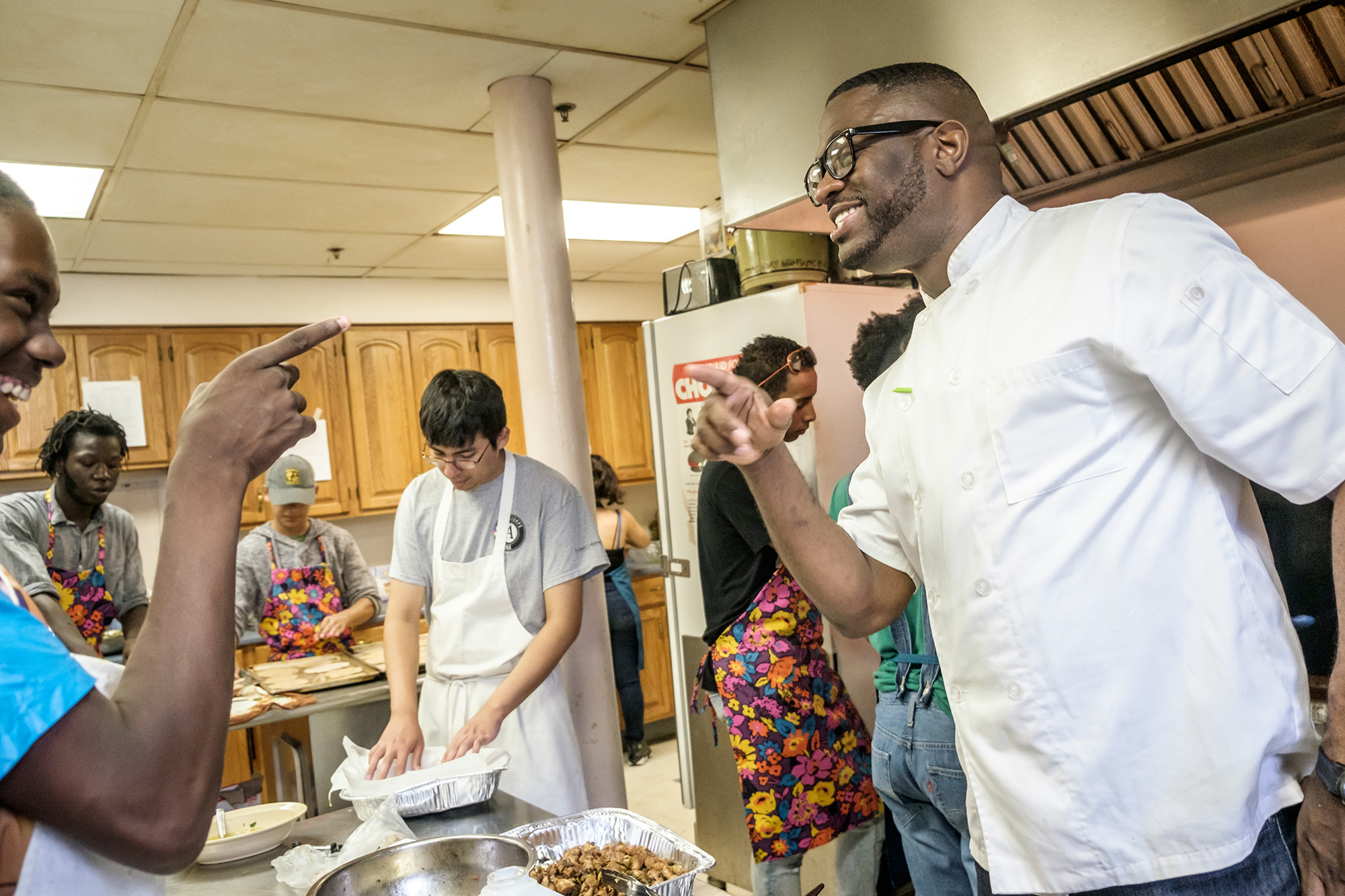 two men smiling at each other while people cook in the kitchen background