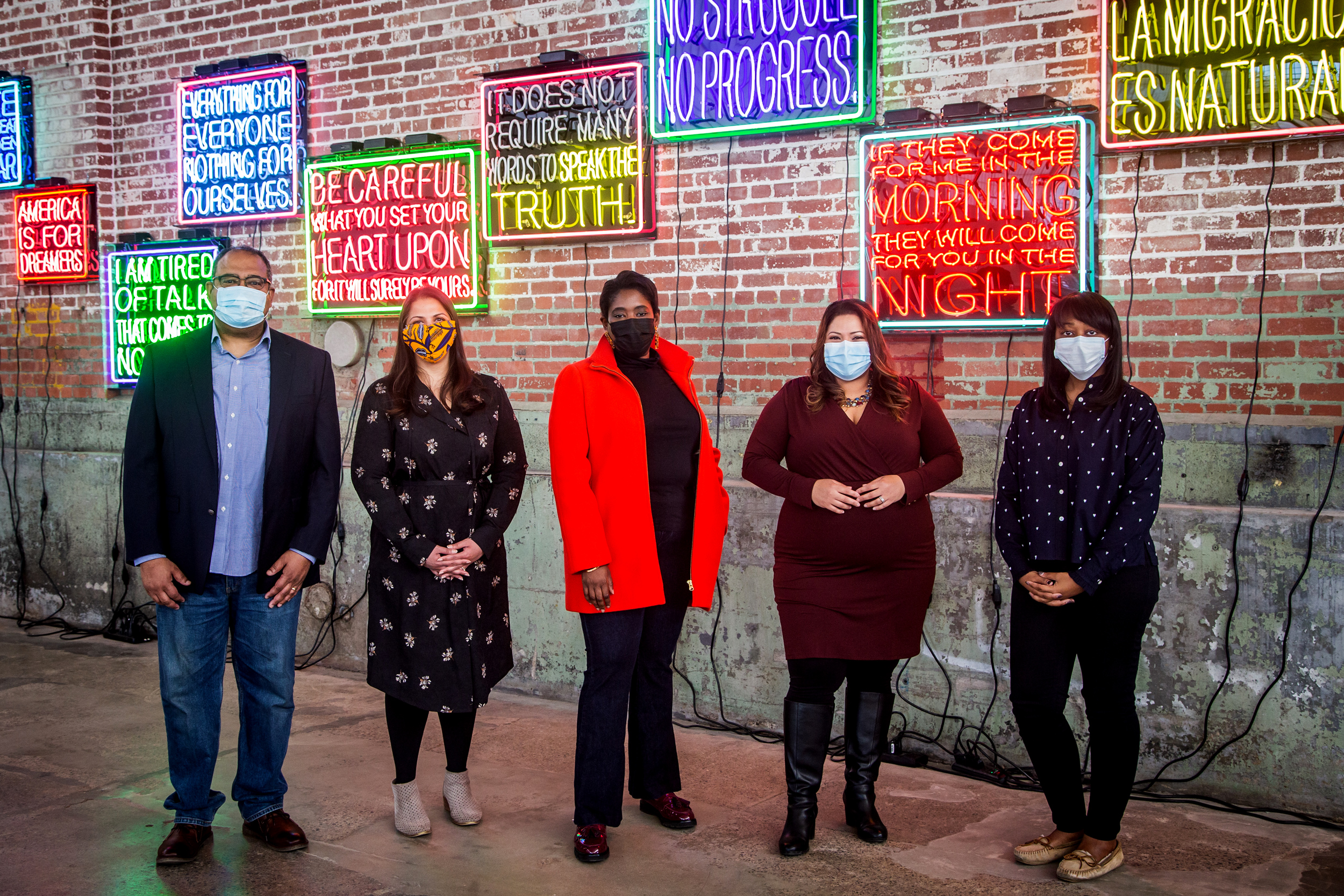 group of people with masks on standing in front of LED signs hanging on the brick wall