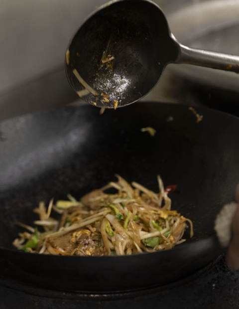 A person skillfully stirring food in a wok, creating a delicious and aromatic dish.