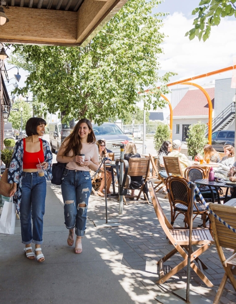 Two women walking along a busy street with patio tables lining the sidewalk