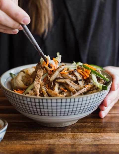 woman eating a stir fry with chopsticks out of a checkered bowl