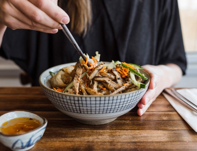 woman eating a stir fry with chopsticks out of a checkered bowl