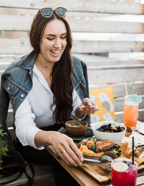 a woman sitting outdoors on a patio at a table set with dinner and cocktails