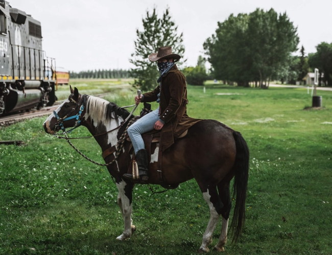 A man dressed as a cowboy on a horse standing beside a stagecoach train