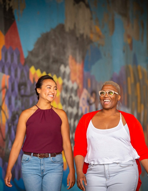 two women walking downtown in front of an art wall