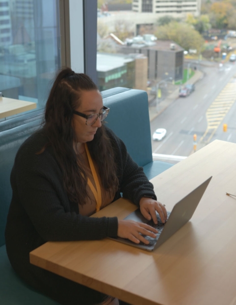 woman working on her laptop at a bench seating area at 7 Shifts