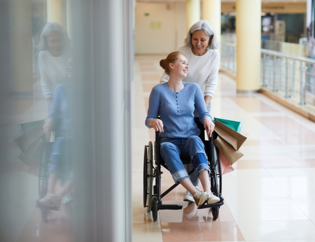 A woman pushing another women in a wheelchair in an indoor public space