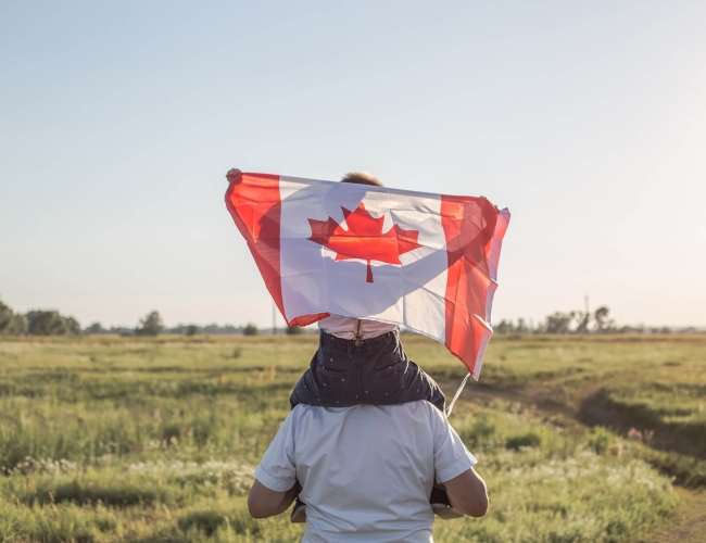 Child holding Canadian flag sitting on someones shoulders