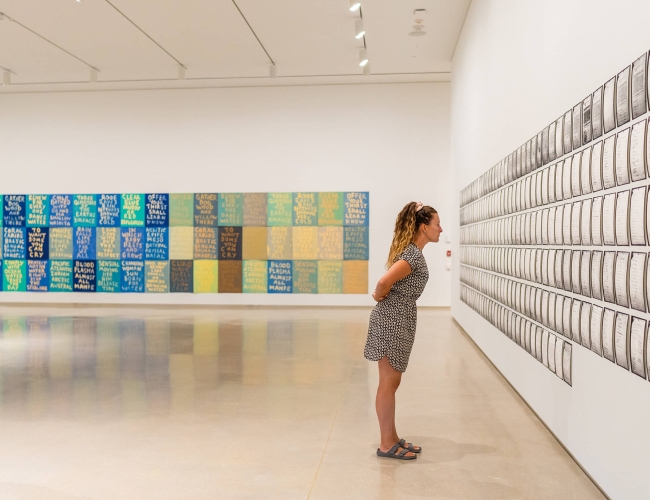 Woman with her arms behind her back, looking at art on a wall in a gallery