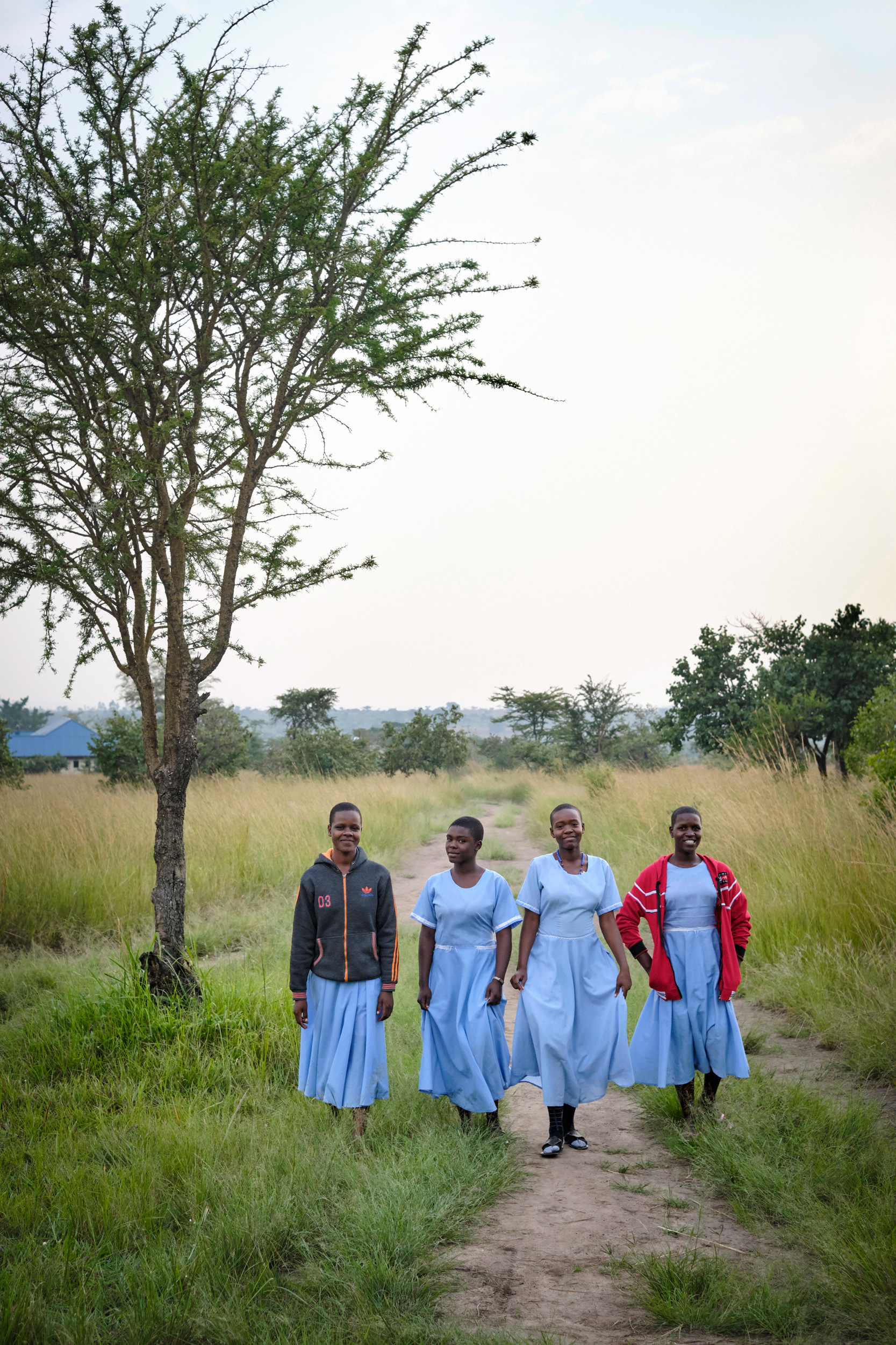 group of girls with long blue dresses on walking through a grass field