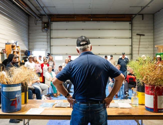 Photo of producer sharing the grains that they grow at their farm to guests in their equipment shed. 