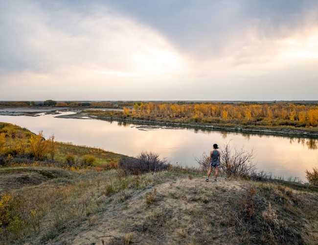 A woman standing on a large rock overlooking a river in the fall